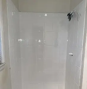 White tiled shower stall with shower head and faucet.
