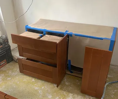 Brown wooden cabinets with drawers open, covered with paper and blue tape.