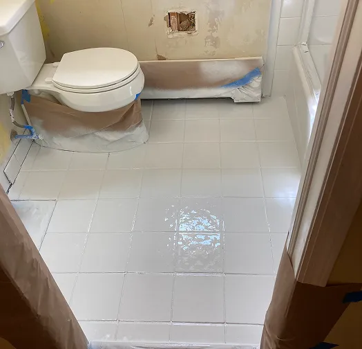 Bathroom renovation with white tiled floor and toilet covered in protective sheeting.