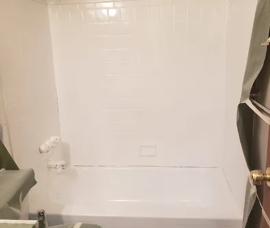 White bathtub and tiled shower walls with protective sheeting on the right.