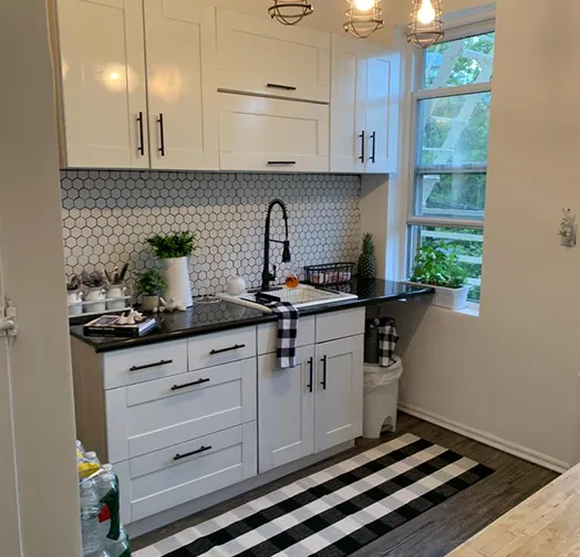 White kitchen with black granite countertops, hexagonal tile backsplash, and a black faucet.