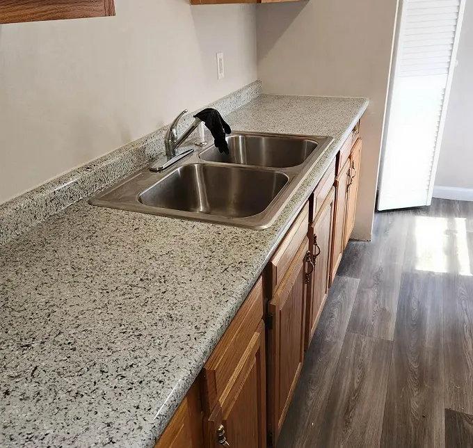 Kitchen counter with double sink and faucet, wooden cabinets, and wood-look flooring.
