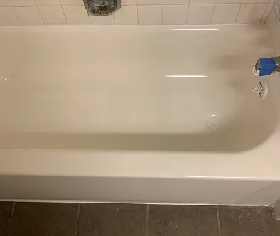 White bathtub with tiled walls and dark floor tiles.