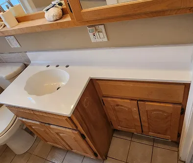 Bathroom vanity with white countertop, sink, and wooden cabinets.