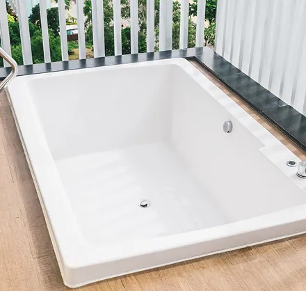 White bathtub on a wooden deck with a railing and trees in the background.