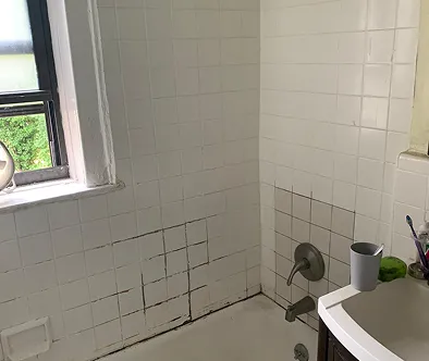 The image depicts a bathroom with white tile walls and a window on the left side