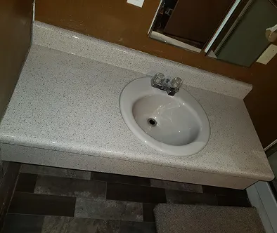 White oval sink with chrome faucet on a speckled countertop.