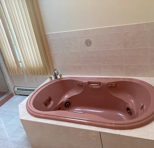 Pink jacuzzi bathtub with chrome fixtures and tiled surround.