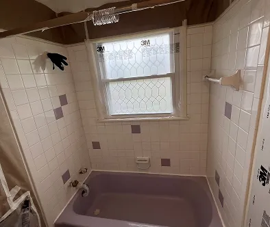 Bathroom with purple tub, white tiled walls, and a window covered in protective film.