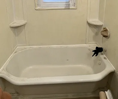 White bathtub with black faucet and shower head against a cream-colored wall.