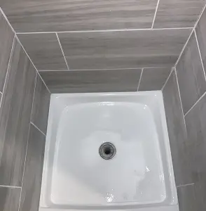 White shower base with gray tiled walls and a drain.