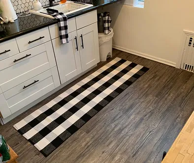 Black and white buffalo check runner rug on a wood-look floor in a kitchen.