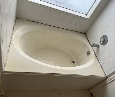 A dirty bathtub with a shower faucet and tiled walls.