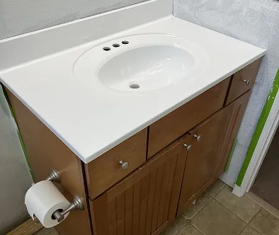 Bathroom vanity with white countertop, sink, and wooden cabinets.