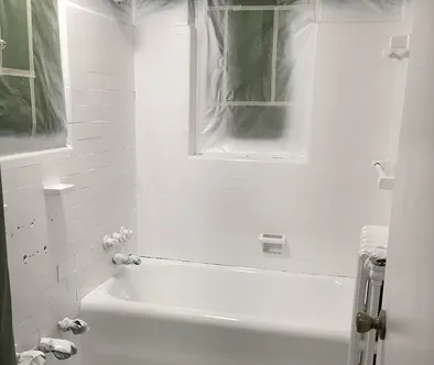 White bathtub and shower area covered in plastic sheeting and drop cloths during renovation.