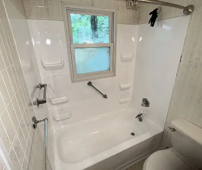 White bathtub with a window above and a toilet to the right.