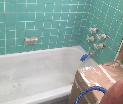 Bathtub with turquoise tile walls and a blue glove reaching for the faucet.