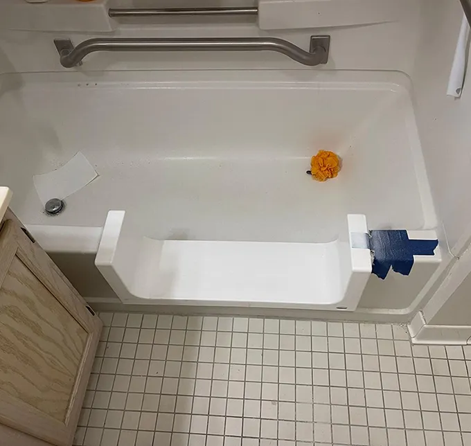 White bathtub with grab bar, shower caddy, and a step insert with blue tape.